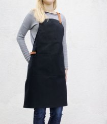 Czarny fartuch barmański ze skórzanymi elementami na blondynce w szarym swetrze i dżinsach, elegancki design z kieszenią i regulowanymi paskami