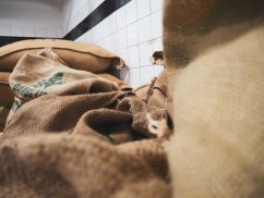 Szczegół jutowych worków po kawie w brązowym kolorze z nadrukowanymi napisami ułożonymi na podłodze obok białej ściany z kafelkami