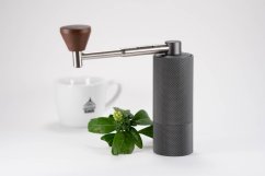 Timemore Nano Grinder mlýnek s rozloženou kovovou klikou a dřevěnou rukojetí vedle bílého porcelánového hrnku s čajovou lžičkou