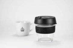 KeepCup Brew Black S 227 ml schwarzer Glasbecher mit schwarzem Deckel neben weißer Porzellanbecher mit Teebeutel auf weißem Hintergrund