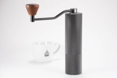 Ruční mlýnek kávy Timemore Slim Plus s černým tělem a hnědou dřevěnou rukojetí, vedle bílého porcelánového šálku na kávu