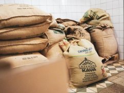 Brązowe worki jutowe od kawy z nadrukiem ułożone na kostkowanej posadzce w rogu pomieszczenia z białymi kafelkami na ścianach