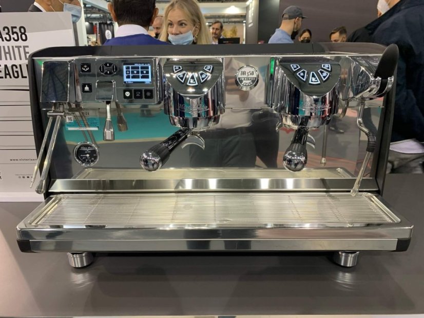 Victoria Arduino White Eagle 358 v provozním prostředí na výstavě s návštěvníky pozorujícími profesionální kávovar s dvěma hlavami