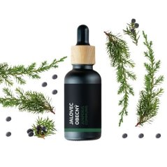 Bottiglia di vetro nero con tappo in legno contenente olio essenziale di ginepro, circondata da fresche ramette verdi di ginepro Bottiglia di vetro nero con tappo in legno contenente olio essenziale di ginepro, circondata da fresche ramette verdi di ginepro