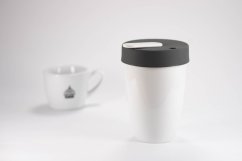 Loveramics Nomad White Thermotasse mit dunkelgrauem Deckel neben verschwommener weißer Tasse mit Logo auf hellgrauem Hintergrund