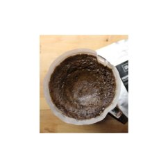 Käytetty Hario V60-01 muovinen tippukeitin paperisella suodattimella, jossa jauhettua kahvia ja jäämiä puisella alustalla