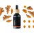 Frasco de vidrio negro con tapón de madera que contiene aceite esencial de cúrcuma BIO, rodeado de raíces frescas de cúrcuma y rodajas naranjas