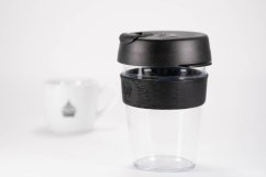 KeepCup Original Clear Black Detail - transparentes Kunststoffgefäß mit schwarzem Deckel und schwarzem Schutzband, Seitenansicht mit unscharfem Hintergrund