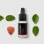 Botella de vidrio negro con gotero que contiene aceite esencial de ashwaganda rodeada de hojas verdes y hoja otoñal roja sobre fondo blanco