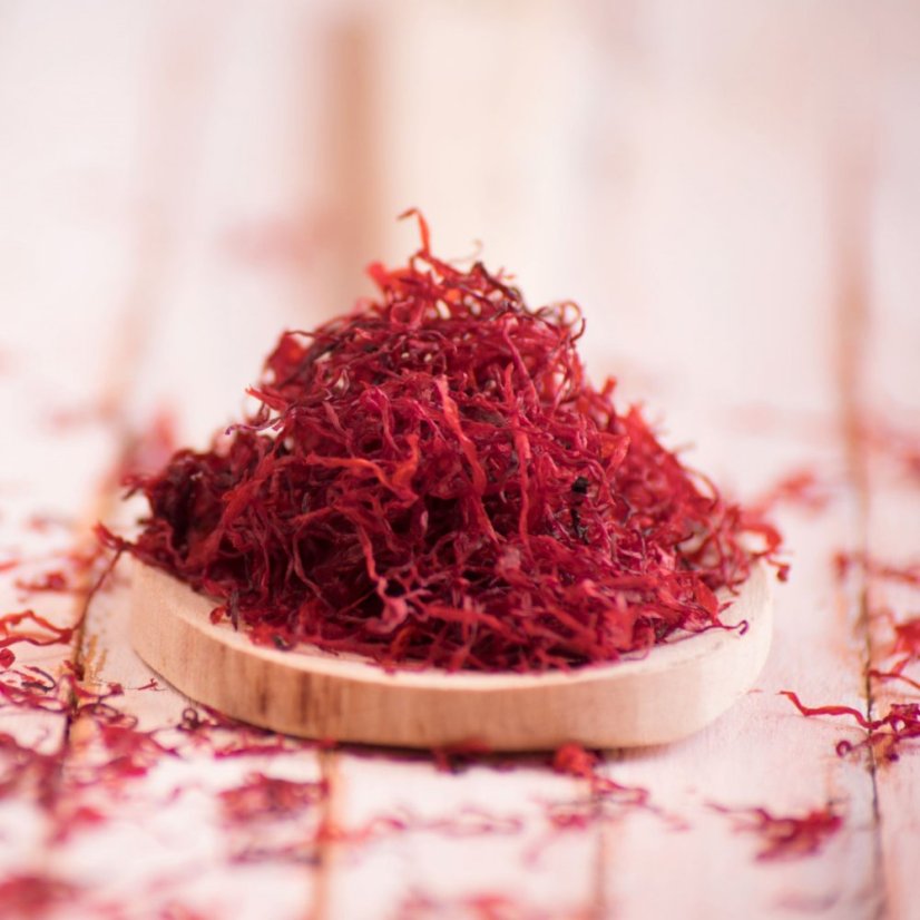 Hromádka sušených červených šafránových nití na dřevěné lžičce - klíčová složka přírodního ajurvédského Kumkumadi oleje
