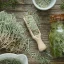 Sušené světle zelené cypřišové větvičky v bílé misce a dřevěné lžíci, sklenice s olejem na dřevěném rustikálním povrchu pro aromaterapii