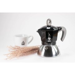 Musta Bialetti-moka-astia valkoisen kupin ja kuivattujen ruohoklasien kanssa luoden viihtyisän kahvihetken