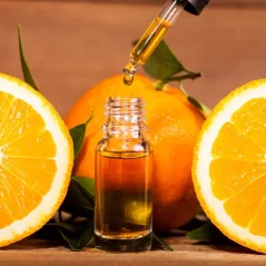 Pipetta di vetro con goccia di olio essenziale d'arancia dorato sopra piccola bottiglia marrone accanto a arance tagliate a metà Pipetta di vetro con goccia di olio essenziale d'arancia dorato sopra piccola bottiglia marrone accanto a arance tagliate a metà