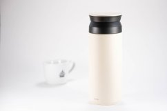 Kinto Travel Tumbler White Thermoskanne mit schwarzem Verschluss auf dem Tisch neben einem verwaschenen weißen Becher im Hintergrund, minimalistischer Stil