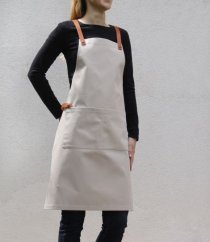 Delantal de barista color arena con tirantes de cuero y cintas de amarre, color beige elegante con triple bolsillo en la parte delantera.