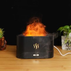 Černý aroma difuzér s imitací plamene s oranžovými plameny vystupujícími z horní části, umístěný na dřevěném stole vedle rostlin Černý aroma difuzér s imitací plamene s oranžovými plameny vystupujícími z horní části, umístěný na dřevěném stole vedle rostlin