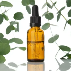 Bernsteinen glazen flesje met druppelaar met goudkleurige BIO eucalyptusolie, omringd door verse groene eucalyptusbladen Bernsteinen glazen flesje met druppelaar met goudkleurige BIO eucalyptusolie, omringd door verse groene eucalyptusbladen