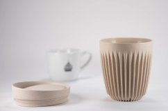 Huskee Natural Becher mit Deckel neben weißer Porzellanmilchkanne, beige mit gerippter Oberfläche zur Temperaturerhaltung