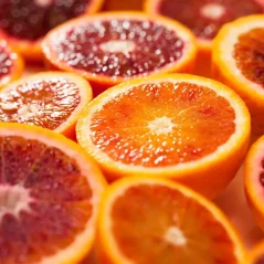 Frische Scheiben einer roten Orange mit intensivem rot-orangefarbenen Fruchtfleisch und gelb-orangefarbener Schale auf glänzender Oberfläche mit Wassertropfen Frische Scheiben einer roten Orange mit intensivem rot-orangefarbenen Fruchtfleisch und gelb-orangefarbener Schale auf glänzender Oberfläche mit Wassertropfen