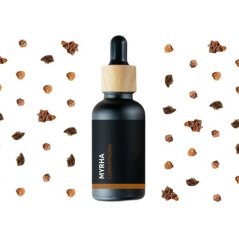 Czarna szklana buteleczka z drewnianą nakrętką i kroplomierzem, zawierająca bio olejek eteryczny Mirra, otoczona drobnymi kawałkami żywicy na białym tle