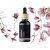 Botella de vidrio negro con tapón de madera que contiene aceite esencial bio de magnolia rodeada de flores de magnolia rosas en ramas